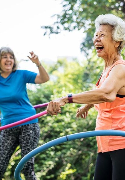 Two older woman smiling, hula hooping, exercising outside